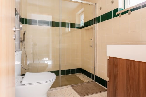 Banheiro moderno com box de vidro, revestimento em tons creme, friso em verde escuro e gabinete de madeira na FC Housing Company
