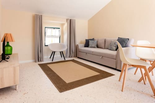 Sala de estar clara em apartamento FC Housing com sofá bege, mesa redonda, cadeiras de madeira e tapete marrom em Abrantes