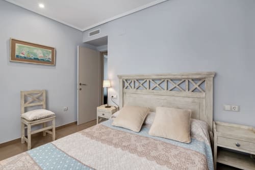 Bright bedroom with wooden X-frame bed, cream pillows, and sea-view apartment in Patacona, Valencia