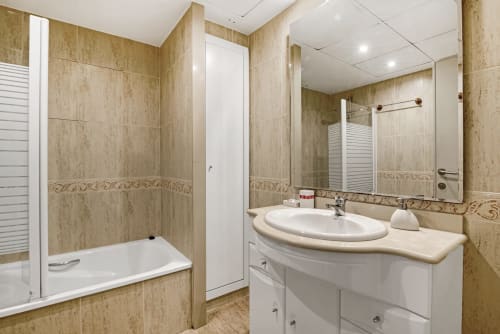 Modern bathroom with beige tile walls, white sink vanity, mirror, and shower enclosure in Valencia beachfront apartment