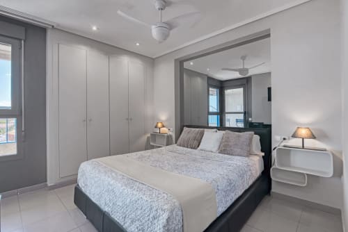 Modern bedroom in Valencia seafront apartment with sea view, queen bed, grey wardrobe, ceiling fan, and balcony access
