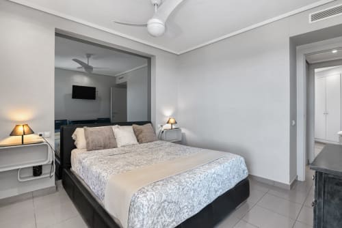 Modern bedroom with black bed, neutral bedding, twin lamps, white ceiling fan, and mirrored wall in Valencia sea-view