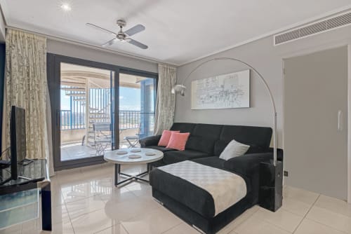 Modern sea-view apartment living room in Valencia with black sofa, white coffee table, and balcony overlooking the coast