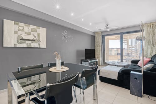 Modern Valencia seafront apartment with dining area, sea view balcony, bedroom, and flat-screen TV in contemporary gray