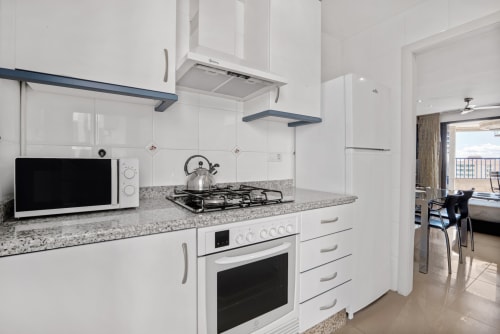Modern white kitchen with granite countertop, gas stove, microwave, and sea-view balcony access in Valencia apartment