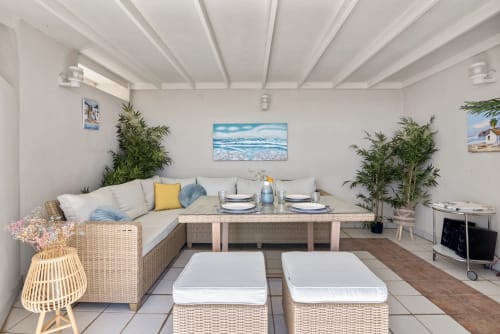 Modern beachfront apartment living room in Valencia with L-shaped seating, dining table, potted plants, and sea view artwork