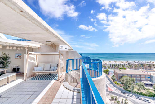 Beachfront penthouse terrace in Valencia with sea views, blue railings, lounge area, and coastal buildings