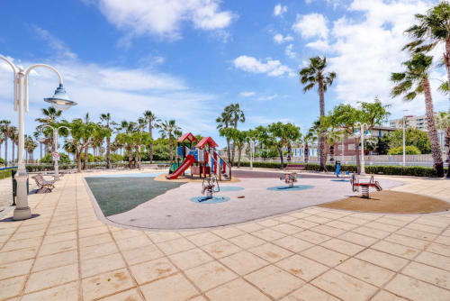 Beachfront playground in Patacona, Valencia with red slide, palm trees, and modern amenities