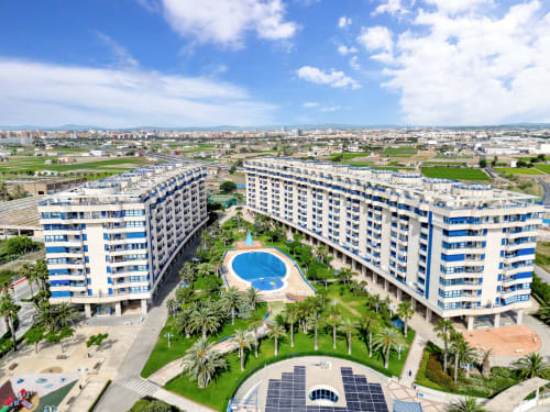 Aerial view of Pataconablue Rentals apartment complex in Valencia with blue-striped buildings, courtyard pool, palm trees,
