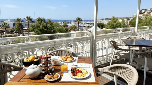 Petit-déjeuner sur la terrasse de l'Hôtel Splendid Cannes avec vue sur la marina, croissants, fruits et paysage méditerranéen