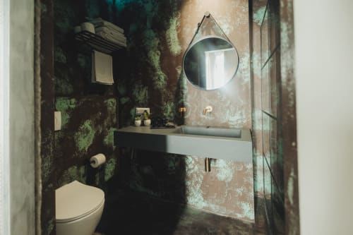 Bagno moderno nell'appartamento Oltre Exclusive a Palermo con pareti a patina industriale verde, specchio rotondo, lavabo bianco, wc