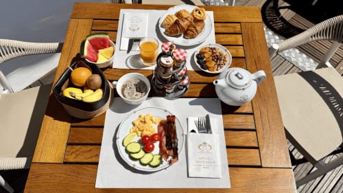 Petit-déjeuner à l'Hôtel Splendide Cannes avec croissants, fruits frais, œufs, bacon et jus sur table en bois
