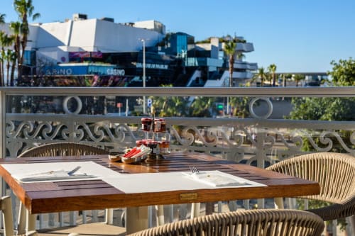 Table de salle à manger extérieure à l'Hôtel Splendid Cannes avec vue sur le casino, palmiers et ciel bleu