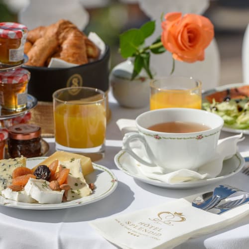 Table de petit-déjeuner de l'Hôtel Splendid Cannes avec fromage, viennoiseries, rose orange, thé et jus