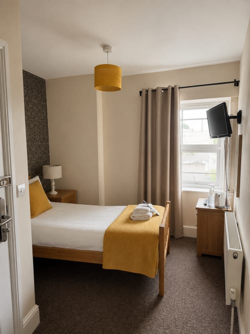 Cozy hotel bedroom at The Cornerhouse Somerset with mustard accents, wooden bed, and wall-mounted TV