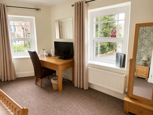 Bright hotel room at The Cornerhouse with wooden desk, TV, two windows overlooking Somerset grounds, cream curtains, and