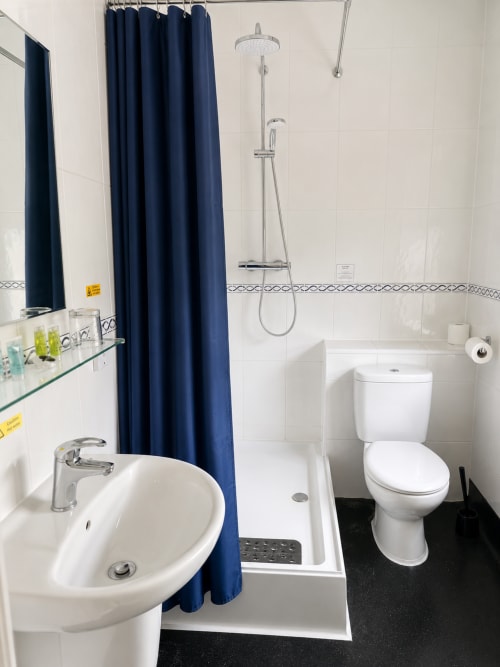 Modern bathroom at The Cornerhouse Somerset with round sink, blue shower curtain, white tiles, and black floor