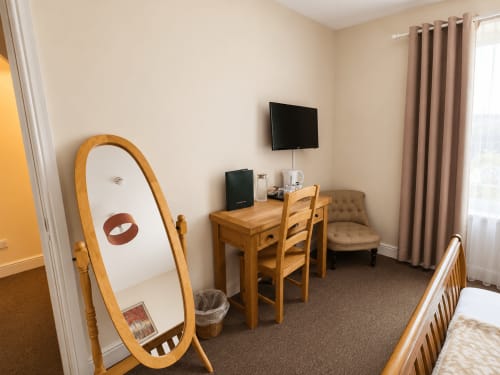 Modern hotel room at The Cornerhouse Somerset with wooden desk, TV, mirror, and comfortable seating by window