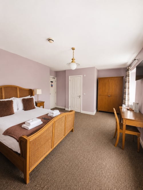 Spacious hotel bedroom at The Cornerhouse Somerset with wooden furniture, pink walls, and modern amenities