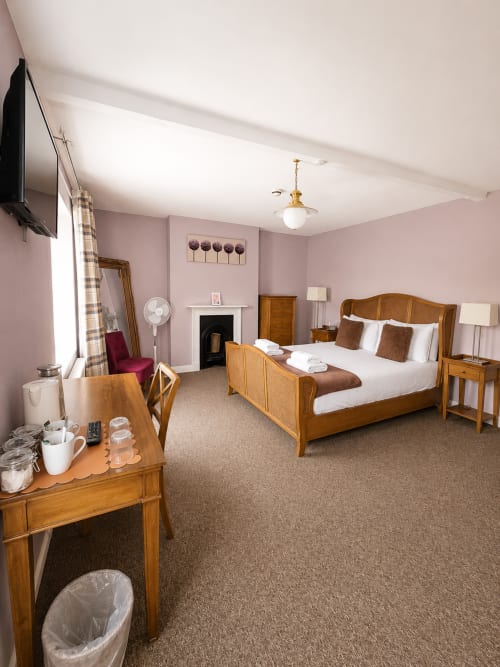 Spacious bedroom at The Cornerhouse Somerset with wooden bed, pink walls, fireplace, and period furnishings
