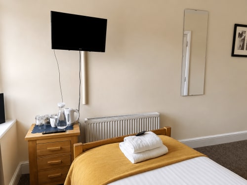 The Cornerhouse single room in Somerset with bed, wooden nightstand, wall-mounted TV, heating radiator, and tea/coffee