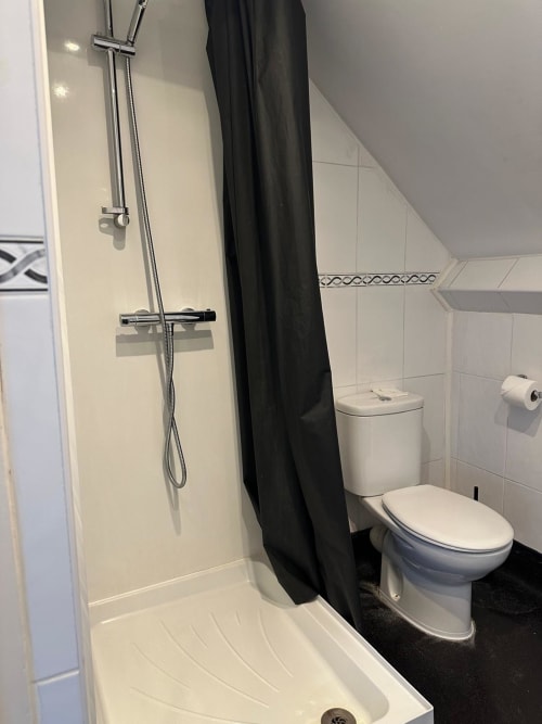 Modern bathroom in Single Room at The Cornerhouse, Somerset featuring shower with black curtain, toilet and white tiling