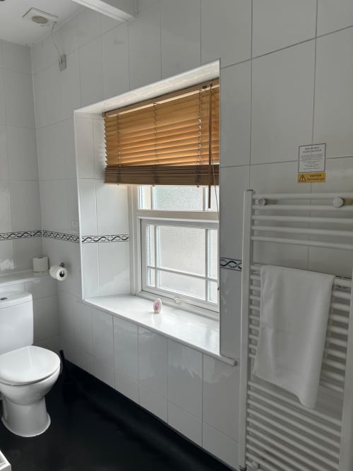 Modern bathroom with white tiled walls, toilet, heated towel rail, and window with wooden blinds at The Cornerhouse hotel in