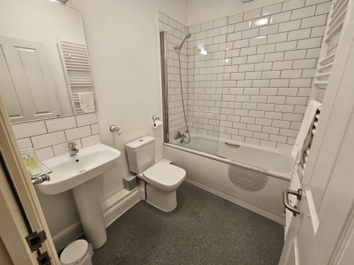 Modern bathroom in The Cornerhouse hotel with white subway tile walls, glass shower enclosure, pedestal sink, and dark