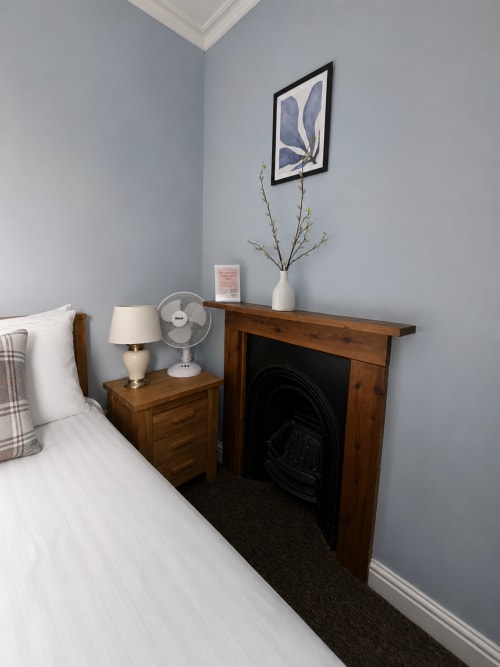 Cozy double room at The Cornerhouse hotel in Somerset with wooden fireplace, bedside table, lamp, and blue botanical artwork