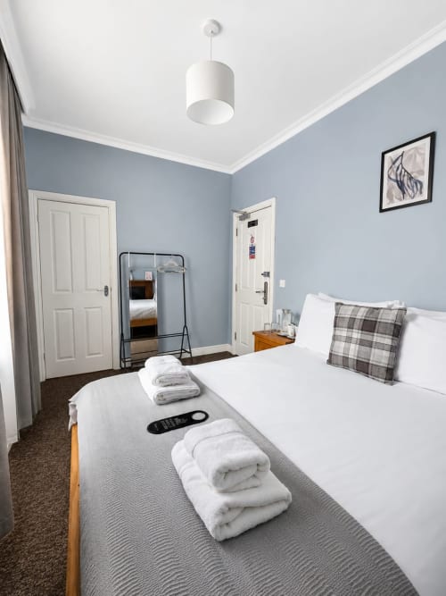 Modern double bedroom at The Cornerhouse, Somerset with blue walls, white bed, towels, and contemporary furnishings