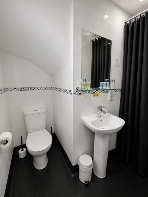 Modern bathroom at The Cornerhouse hotel in Somerset with white tiles, pedestal sink, toilet, and black shower curtain