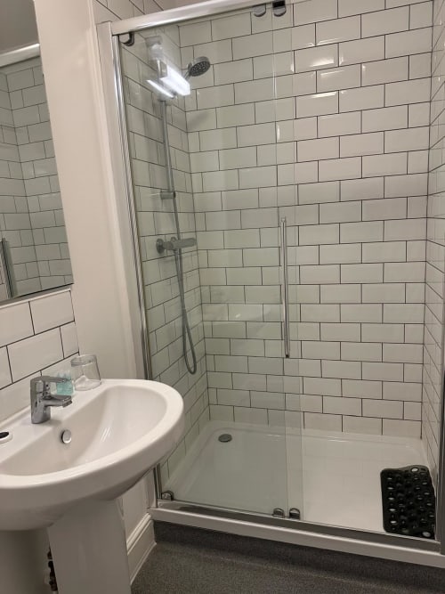 Modern bathroom at The Cornerhouse hotel with white subway tiles, glass shower enclosure, and pedestal sink in Somerset