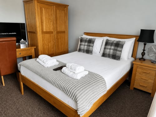 Spacious double bedroom at The Cornerhouse Somerset with wooden furniture, white linens, plaid cushions and hospitality