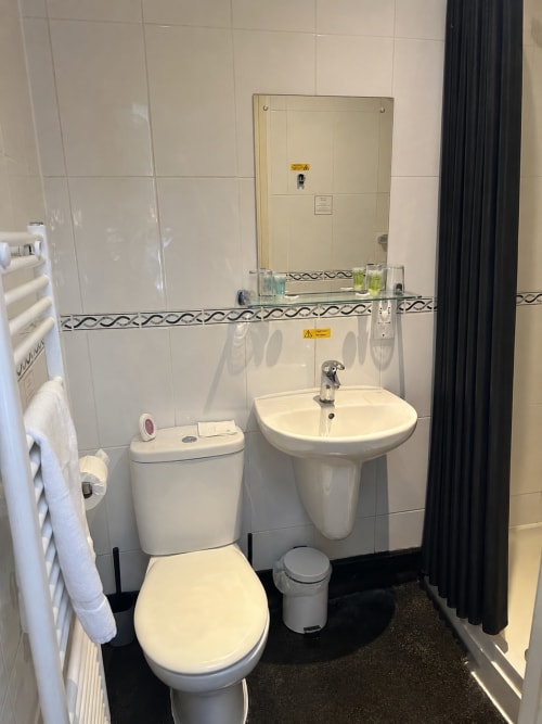 Modern bathroom at The Cornerhouse hotel in Somerset featuring white toilet, pedestal sink, heated towel rack, and tiled