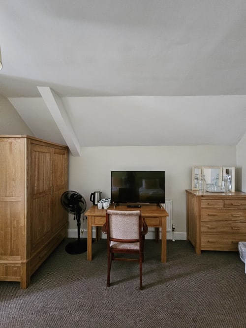 Attic bedroom in The Cornerhouse Somerset hotel with wooden furniture, desk, TV, and fan