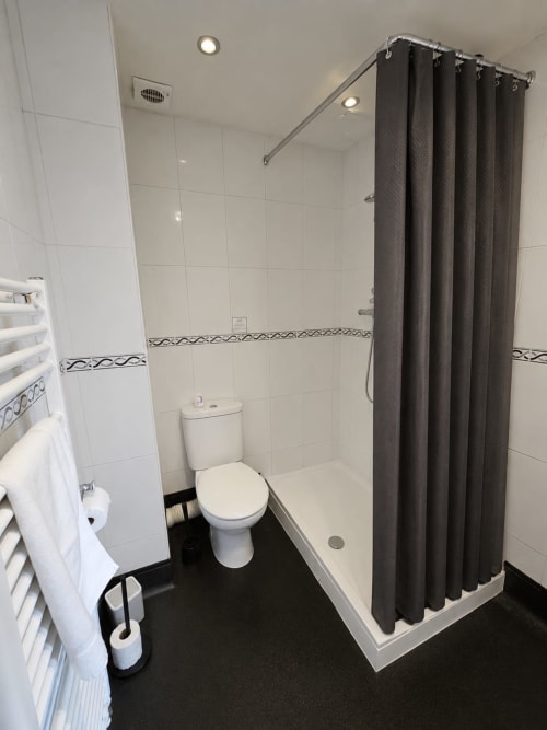 Modern bathroom at The Cornerhouse Somerset with white tiles, dark floor, toilet, and walk-in shower with grey curtain