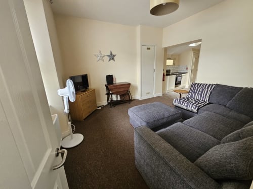 Spacious one-bedroom apartment living area at The Cornerhouse in Frome with gray sofa, wooden desk, and kitchen access