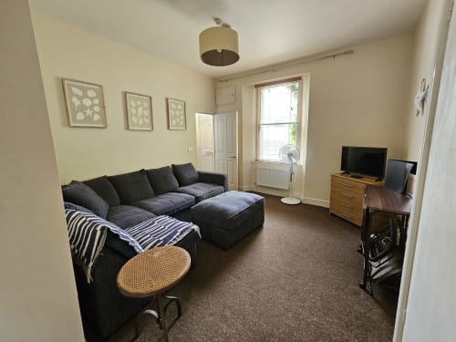 Spacious one-bedroom apartment at The Cornerhouse in Frome featuring dark sectional sofa, wooden TV unit, and cream walls