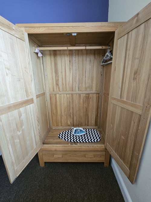 Wooden wardrobe closet in The Cornerhouse apartment showing interior hanging space with clothing hangers and black chevron