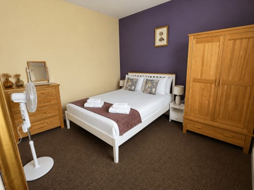 Spacious bedroom at The Cornerhouse apartment in Frome with wooden furniture, purple accent wall, and white bedding