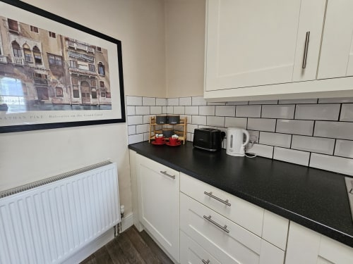 Modern kitchen in The Cornerhouse apartment, Frome, with white cabinetry, black countertop, subway tile backsplash, and