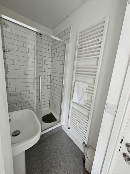 Modern bathroom at The Cornerhouse hotel with white subway tiles, glass shower enclosure, heated towel rack, and dark gray