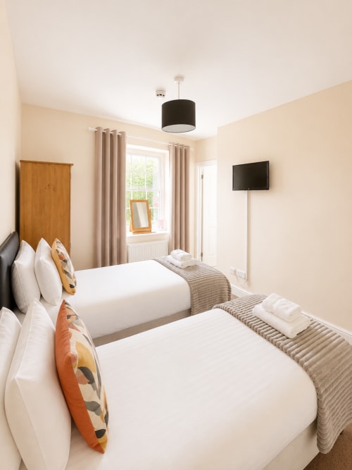 Twin/Double Room at The Cornerhouse in Somerset with two white beds, wooden headboard, beige walls, and TV mounted on the