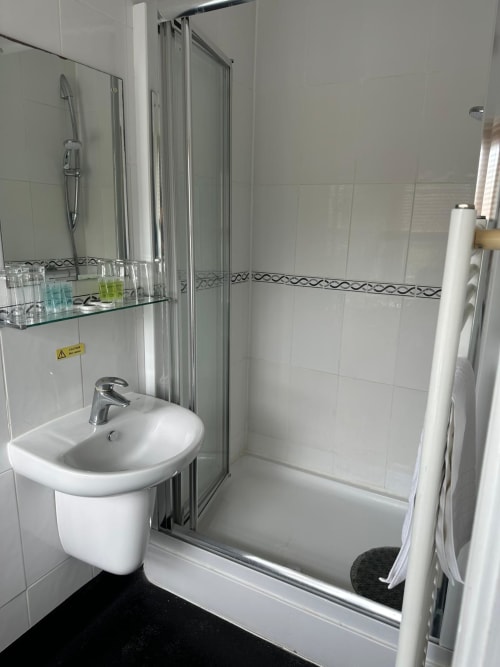 Modern white bathroom with walk-in shower, pedestal sink, and decorative tile border at The Cornerhouse hotel in Somerset