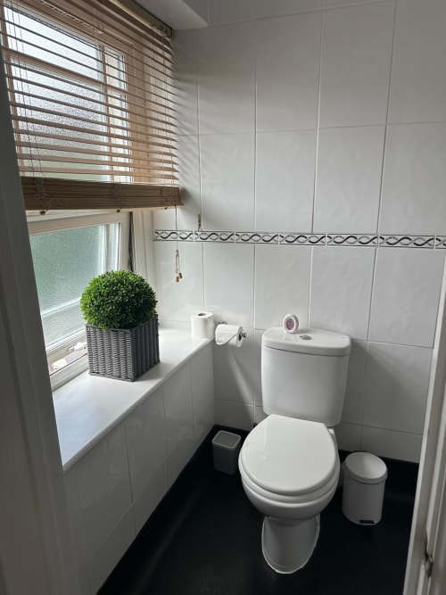 Clean white-tiled bathroom at The Cornerhouse hotel in Somerset with toilet, sink, window, and potted plant decor