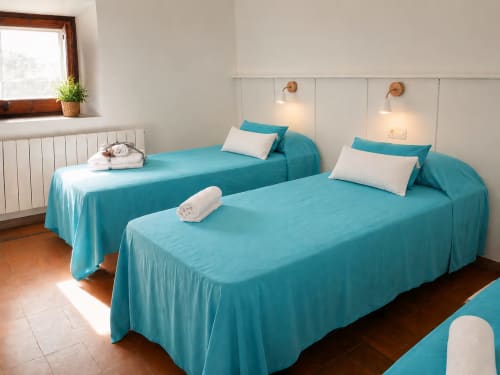 Dos llits bessons amb llençols turquesos en habitació clara de l'hotel Mas Ribas a Palamós, amb vistes al jardí i finestra amb bigues de fusta