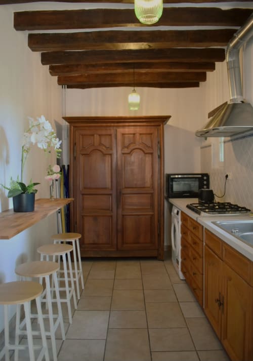Cuisine rustique du Moulin Garnier avec poutres apparentes, mobilier en bois, cuisinière à gaz et bar à Vernou sur