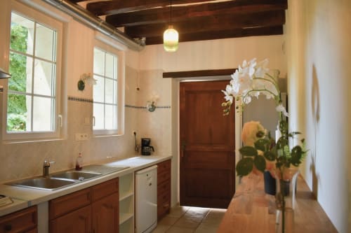 Cuisine moderne au cottage Le Moulin Garnier avec armoires en bois, comptoirs blancs, grandes fenêtres et orchidées blanches