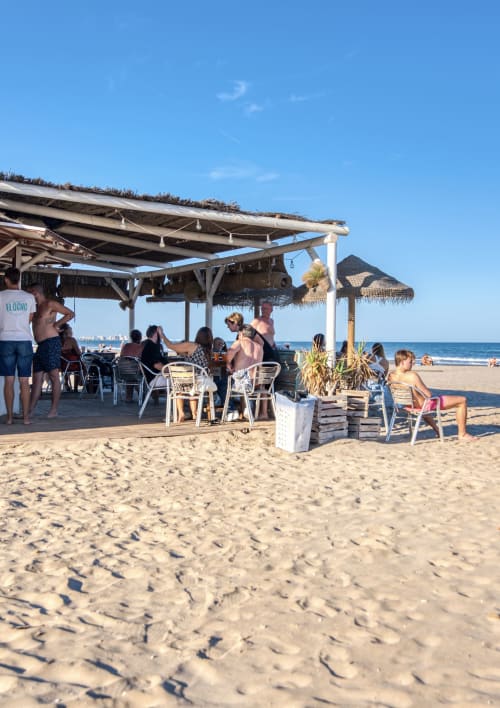 Bar de playa con sombrillas de paja y zona de comedor en Pataconablue Rentals en Valencia, con vistas al Mar Mediterráneo