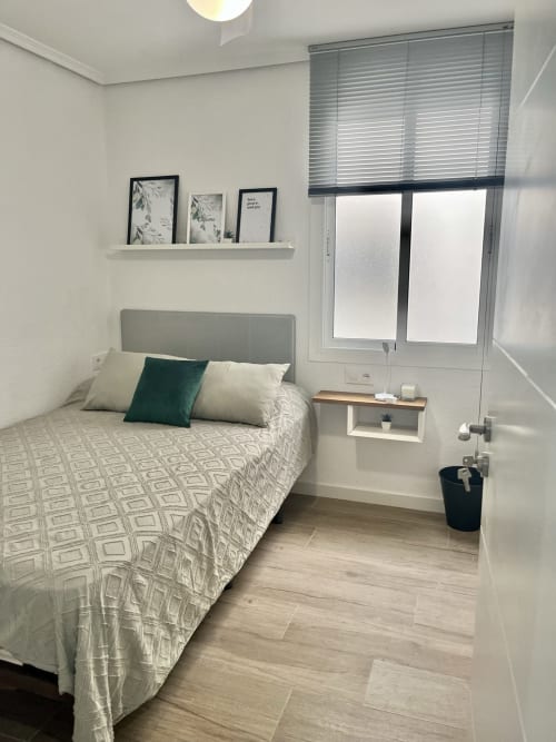 Dormitorio moderno en Valencia con cama cabecero gris, vista a la ciudad a través de puertas de vidrio, estante flotante, diseño minimalista